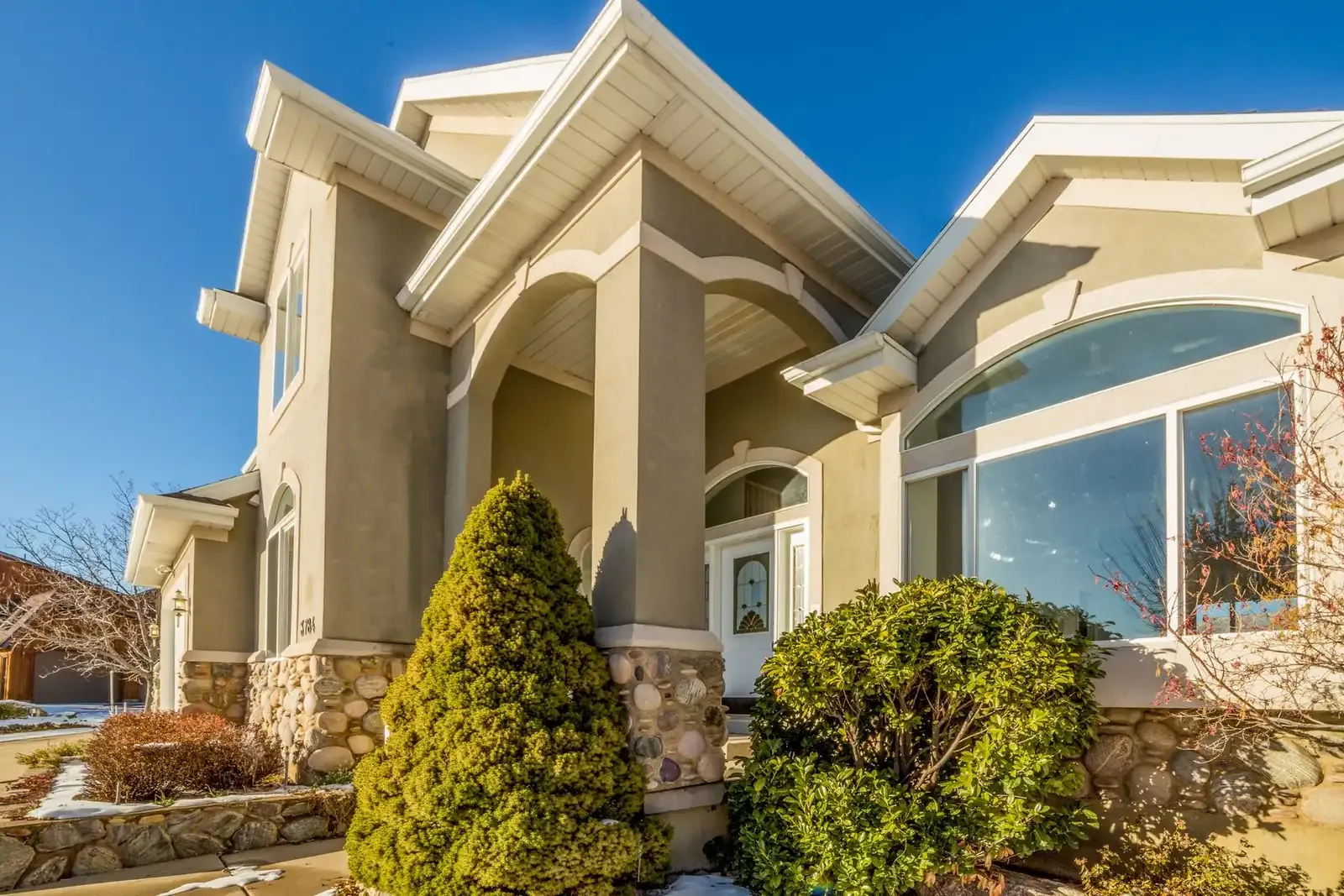 Welcoming stucco and stone home with a landscaped front yard under a blue sky