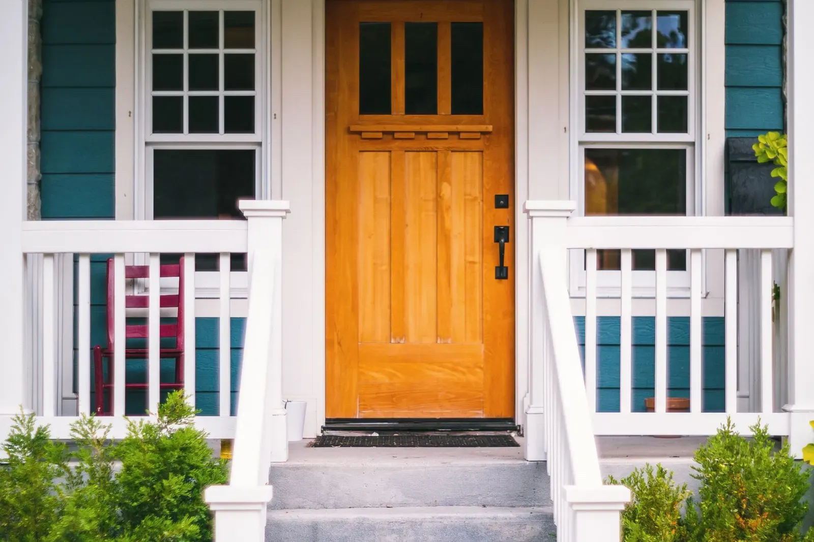 Home front porch with an orange front door, white railings, and flowers